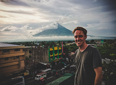 Student Ethan Hughes posing for a photo in Phillipines. Picture taken on a rooftop with a mountain in the background