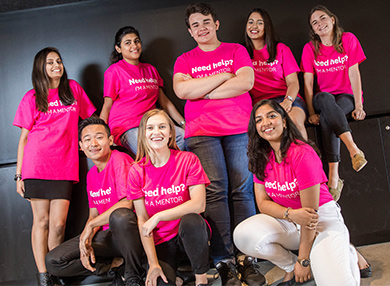 Peer mentors wearing pink shirts huddled for a group photo