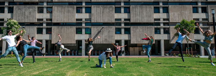 A group of students jumping in the air on the grass in front of a Macquarie University building.
