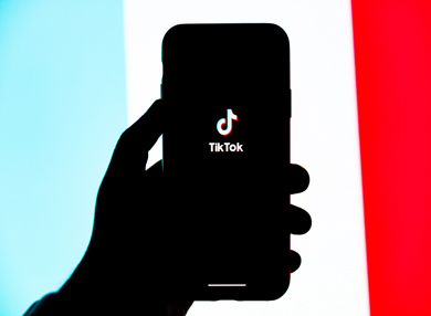 Hnad holding a mobile phone showing the Tik Tok logo.