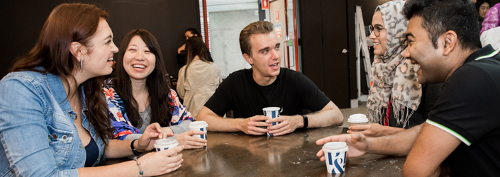 Students chatting and sitting around a wooden table while holding coffee cups
