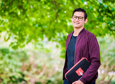 Male student standing outside holding a Macquarie University laptop sleeve.